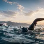 Open Watere Swimmer swimming in an ocean during susent with land just around the corner.