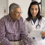 Doctor discussing medical information with a senior patient during a consultation, reviewing details on a digital tablet in a healthcare clinic. The image highlights health insurance planning, preventive healthcare, medical guidance, senior citizen health coverage, and informed healthcare decisions.